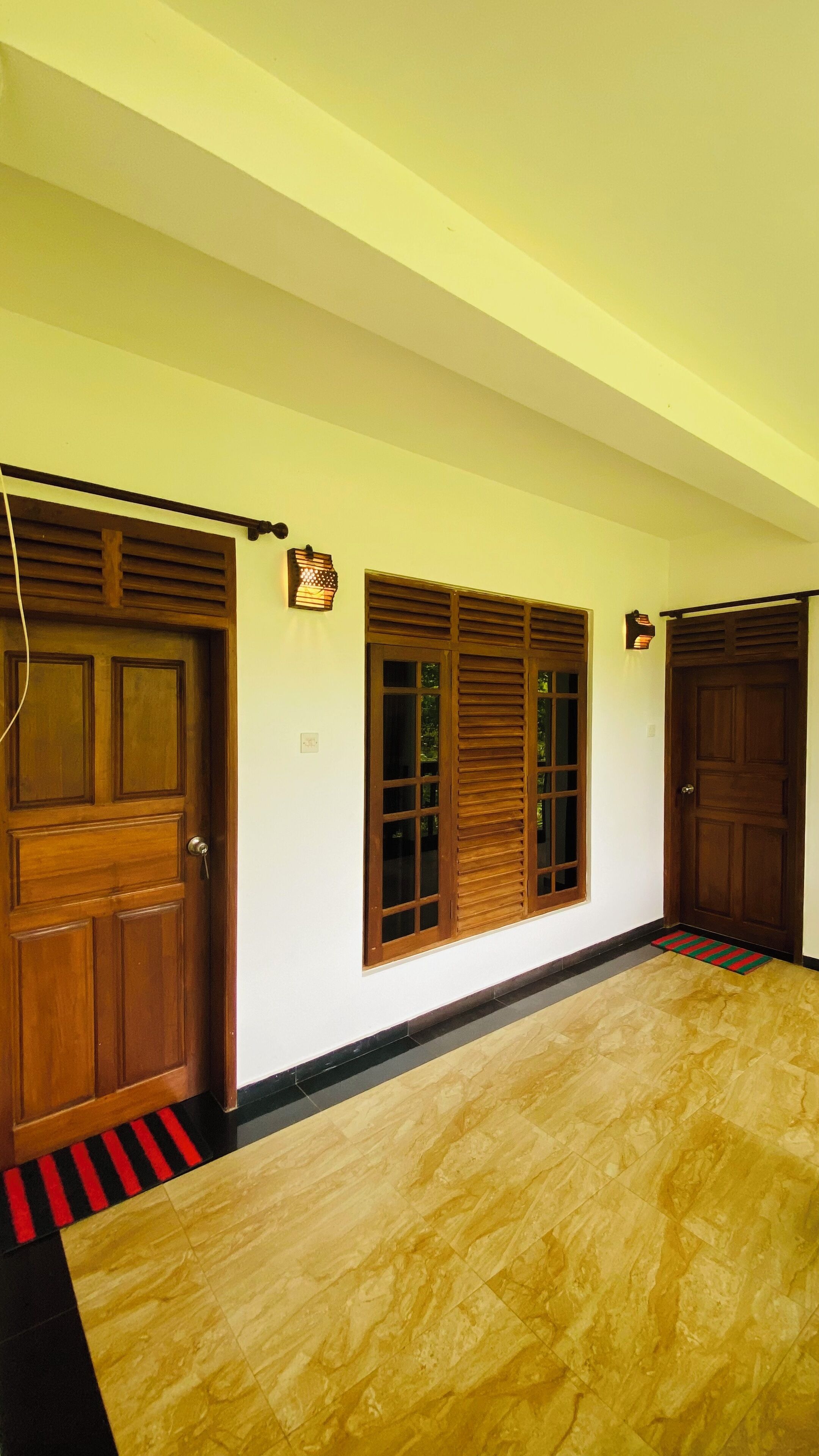 A hallway with wooden doors, a window with shutters, and a tiled floor.