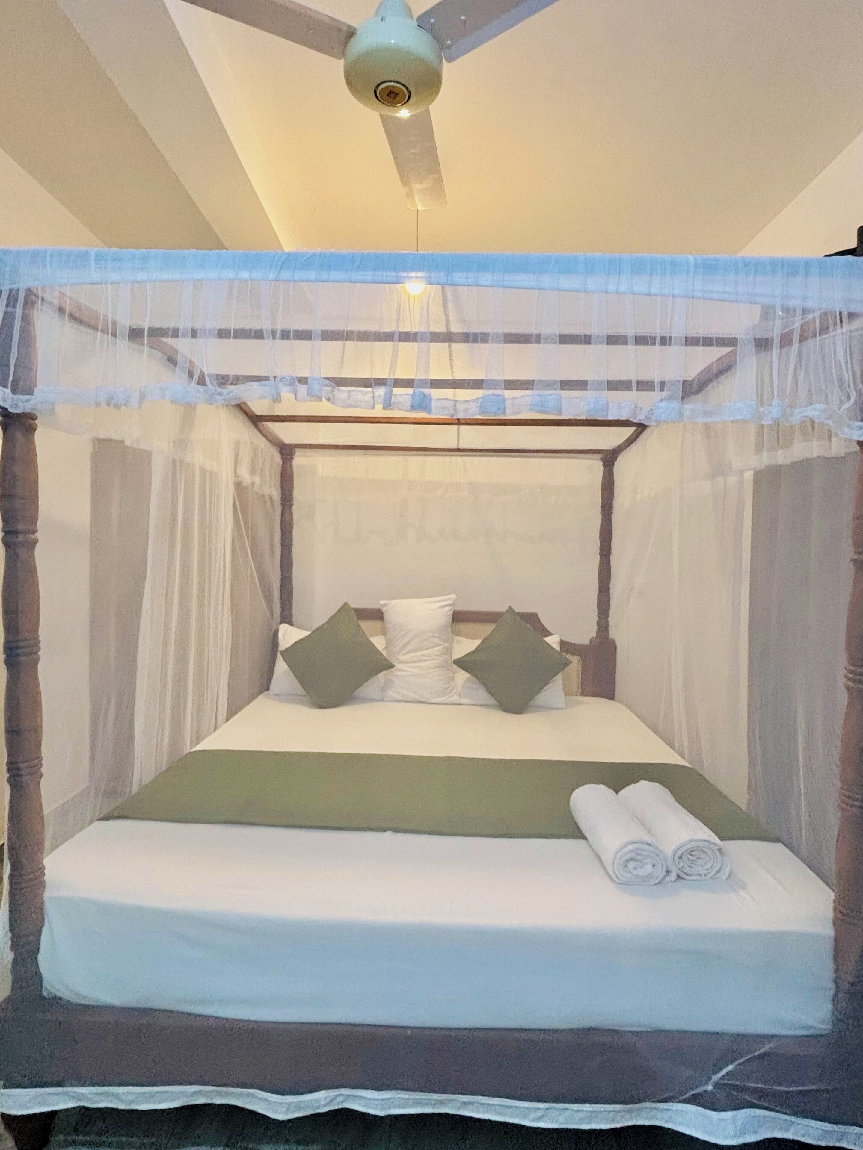 A bed with a canopy, pillows, and rolled towels.