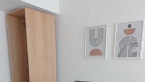 Un dormitorio con cama, ropa de cama gris, una colcha azul, un armario de madera y dos obras de arte abstracto en la pared.