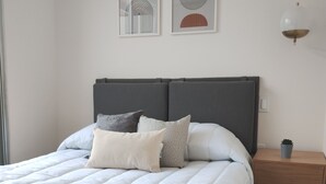 Un dormitorio moderno con una cama grande, cabecera gris y una mesita de noche con lámpara.