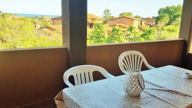 A balcony with a table and chairs, overlooking a residential area with houses and greenery. - AmareSardegna 3 (Muravera - Costa Rei)