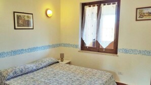 A bedroom with a bed, a nightstand, a wall-mounted lamp, and a window with curtains. - AmareSardegna 3 (Muravera - Costa Rei)