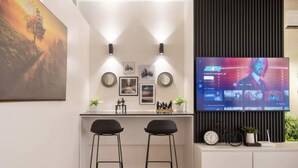 A modern kitchen with two bar stools, a large flat-screen TV mounted on a black panel, and a painting above the counter. - vacationhomesng (Lagos)