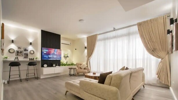 A modern living room with a sofa, a TV, and a bar area with stools. - vacationhomesng (Lagos)