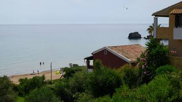 A coastal view with a beach, a red building, and a rocky outcrop in the sea.