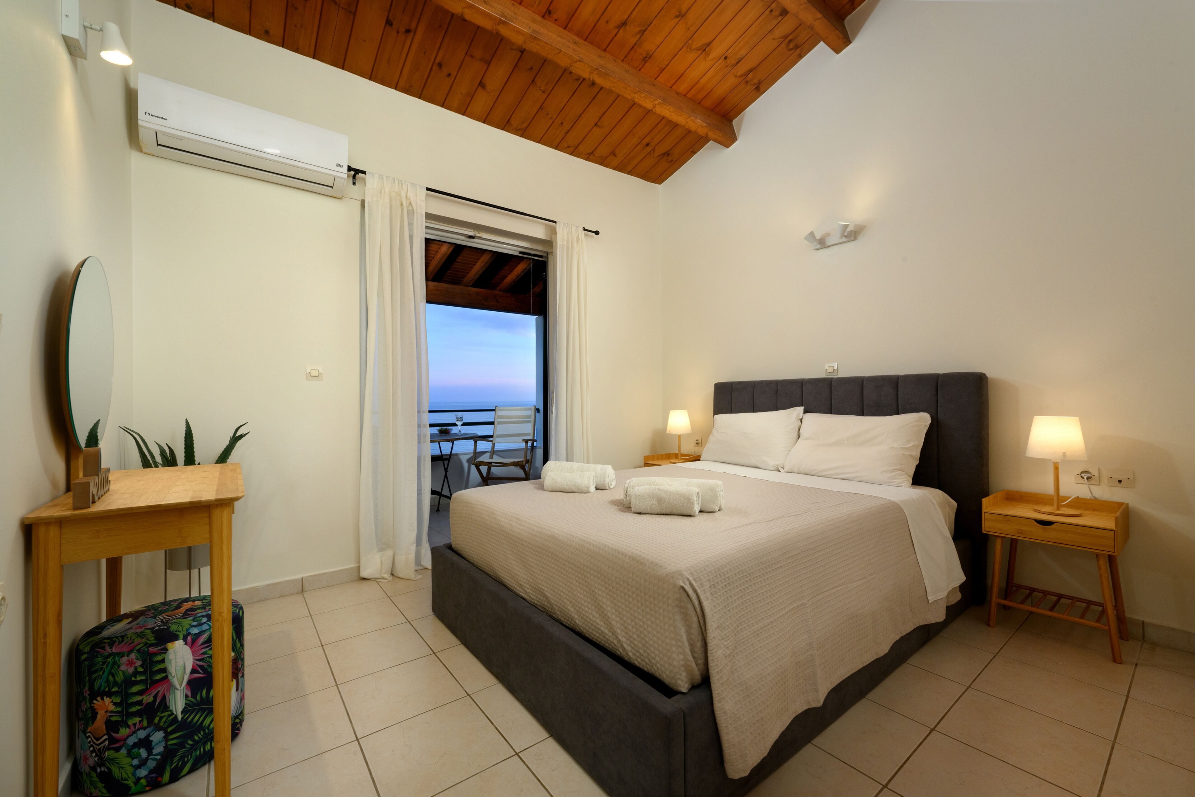 A bedroom with a bed, bedside tables, a mirror, a window with curtains, and a view of the outdoors.