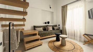 A modern living room with a wooden staircase, a sofa with cushions, a round rug, and a TV mounted on the wall.