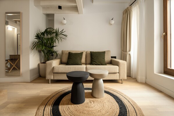 A modern living room with a sofa, two side tables, a potted plant, and a large mirror.