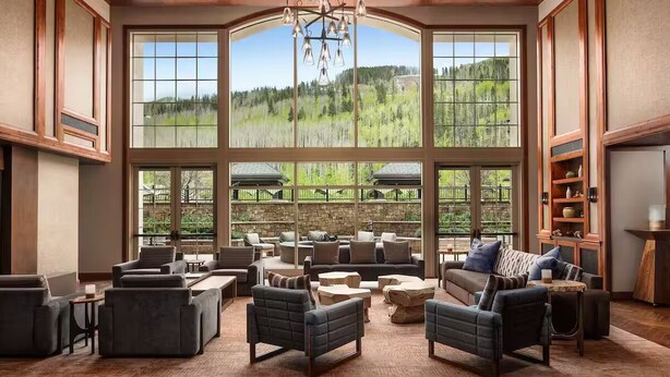 A spacious living room with large windows, comfortable seating, and a view of a forested area. - Ritz-Carlton Residence Club Vail, CO Luxury 3 Bedroom 
Condo Resort- Sleeps 8 (Vail)