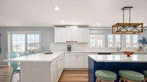 A modern kitchen with white cabinetry, a large island with stools, and a hanging light fixture. - Five Bedroom Waterfront Home with Lots of Space (Ocean City)