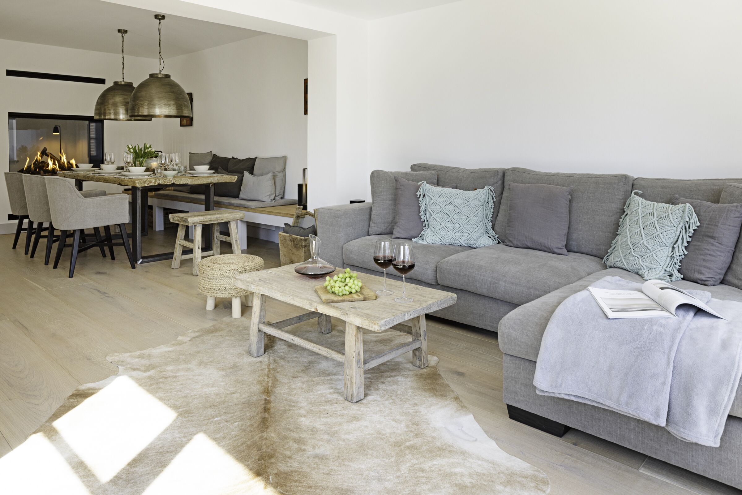 Una sala de estar moderna con un sofá gris, una mesa de centro de madera y una zona de comedor con una mesa y sillas de madera.