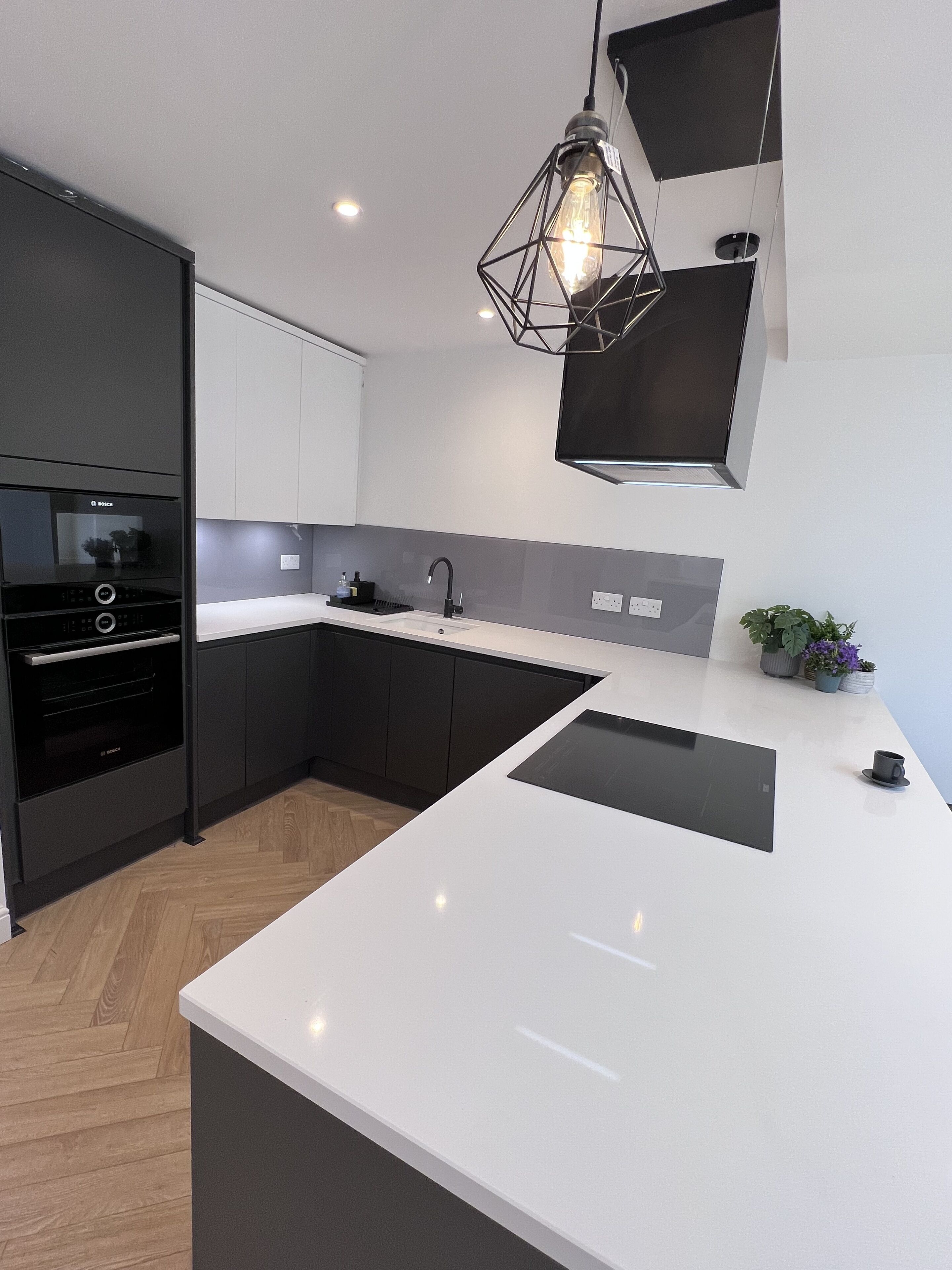 A modern kitchen with a central island, black cabinetry, a Bosch oven, and a pendant light.
