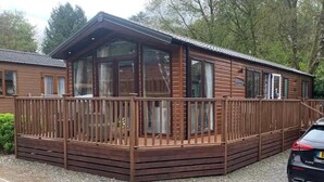 A wooden cabin with a balcony, large windows, and a car parked nearby. - Stunning 3-bed Lodge in Windermere (Windermere)
