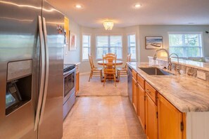 A modern kitchen with a stainless steel refrigerator, wooden dining table, and a marble countertop.