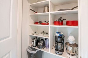 A kitchen with white shelves, containing various kitchenware and appliances like pots, pans, a coffee maker, and a blender.
