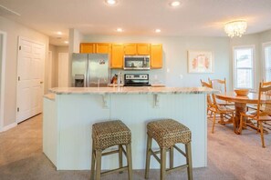 Una cocina con armarios de madera, un refrigerador, un microondas y un comedor con mesa y sillas.
