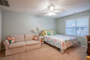 A bedroom with a bed, a beige sofa, a ceiling fan, and a window with blinds.