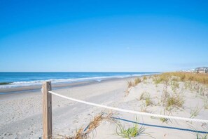 Une plage délimitée par une barrière de cordes, des dunes de sable et un ciel bleu dégagé.