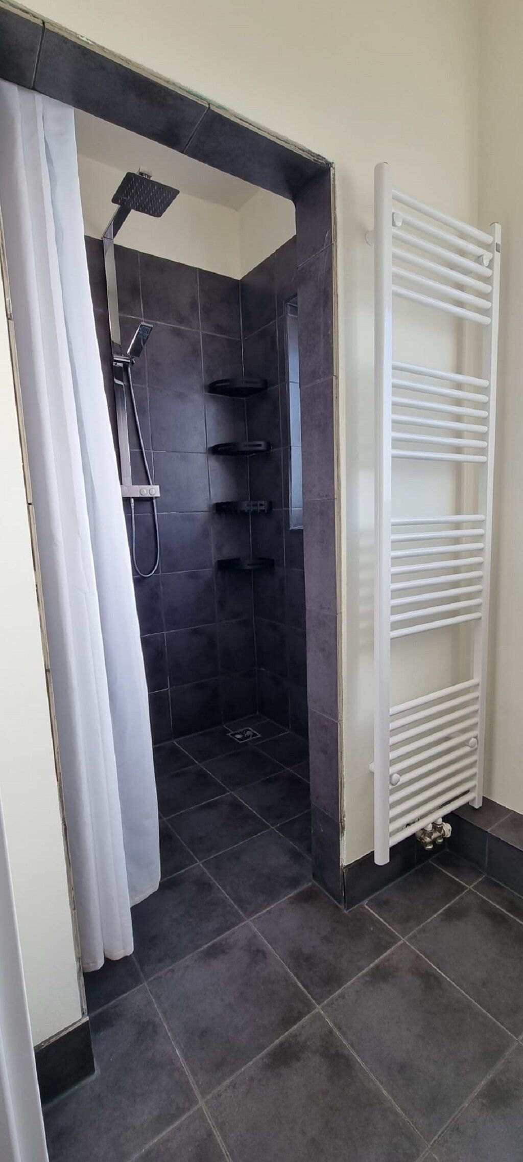A bathroom with a shower area, a white towel rack, and a tiled floor.