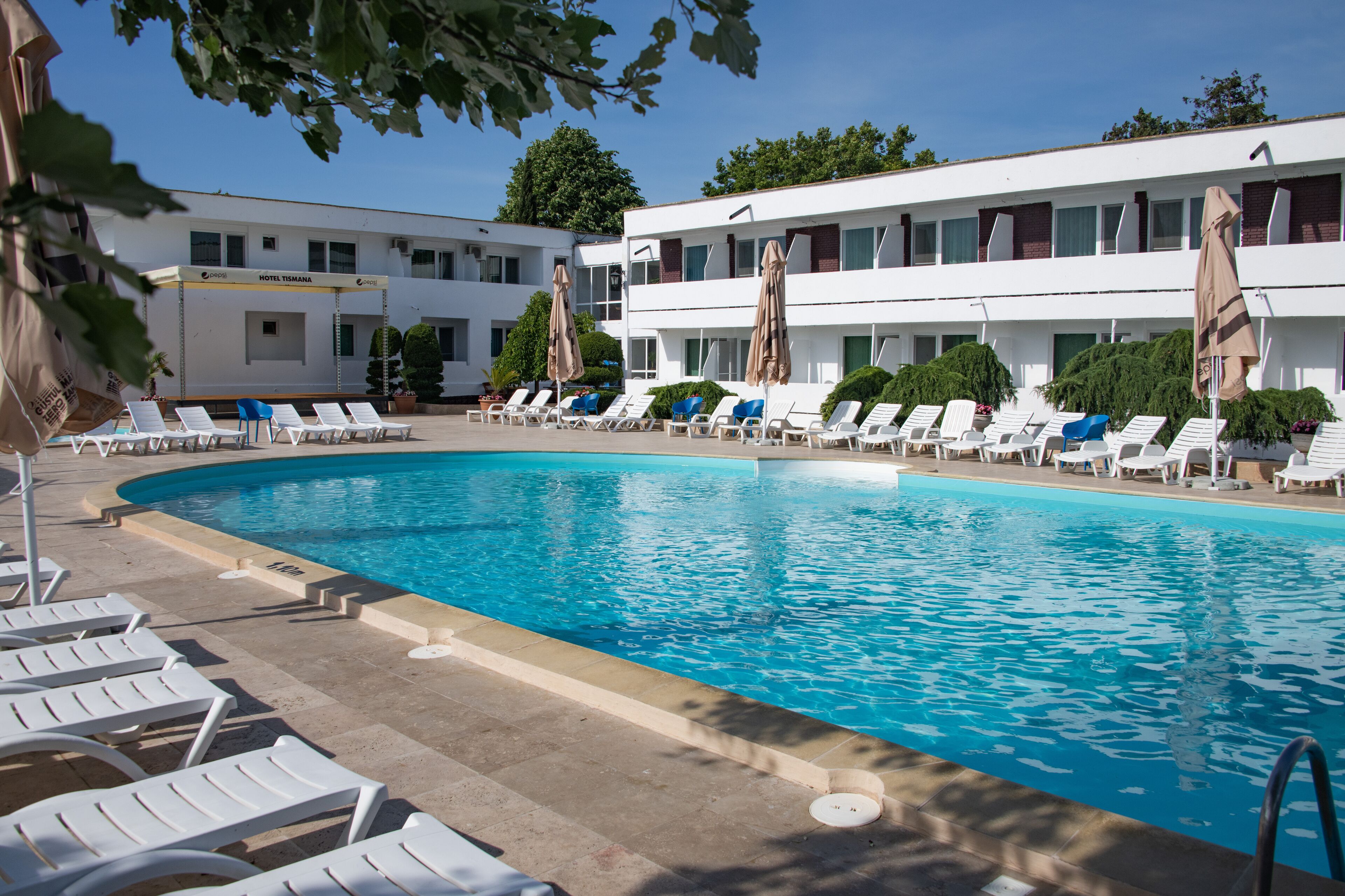 A swimming pool with lounge chairs and umbrellas, surrounded by a hotel building with multiple floors and windows.