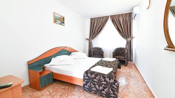 Una habitación de hotel con una cama, dos sillones, una mesita, un escritorio y un cuadro en la pared.