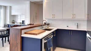A modern kitchen with white and dark blue cabinetry, a wooden island with a cutting board, and a built-in dishwasher. - Ski-In/Ski-Out Mont-Blanc Condo w/ Pool & Lake Access (Mont-Blanc)