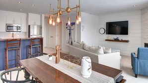 A modern kitchen with white cabinets, a stainless steel microwave, and a wooden dining table with a white vase. - Ski-In/Ski-Out Mont-Blanc Condo w/ Pool & Lake Access (Mont-Blanc)