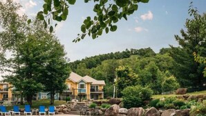 A hotel with a two-story structure, outdoor seating area with blue chairs, and a natural landscape with trees and rocks. - Ski-In/Ski-Out Mont-Blanc Condo w/ Pool & Lake Access (Mont-Blanc)