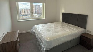 Un dormitorio con una cama grande, una ventana con vistas a la ciudad, un aparador de madera y una mesita de noche.