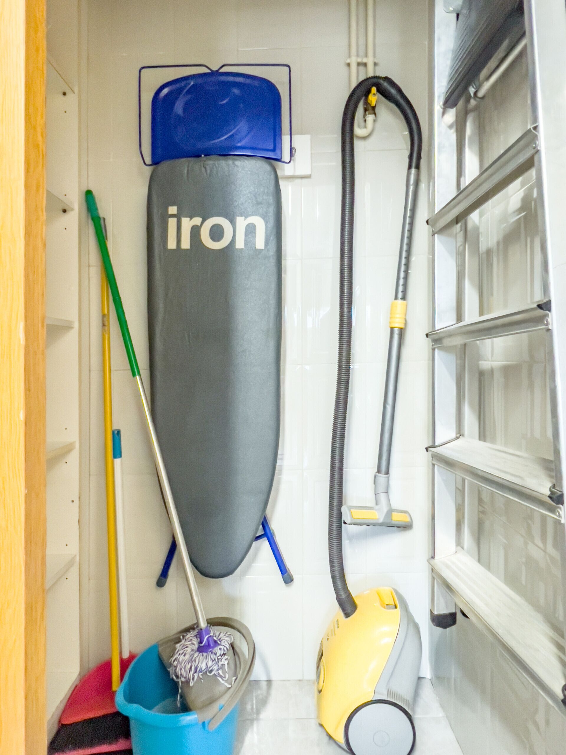 A compact storage area with a vacuum cleaner, a mop, a dustpan, and a cleaning iron.