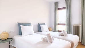 Hotellihuone, jossa on kaksi sänkyä, pieni pöytä, lamppu ja ikkuna, jossa on verhot.