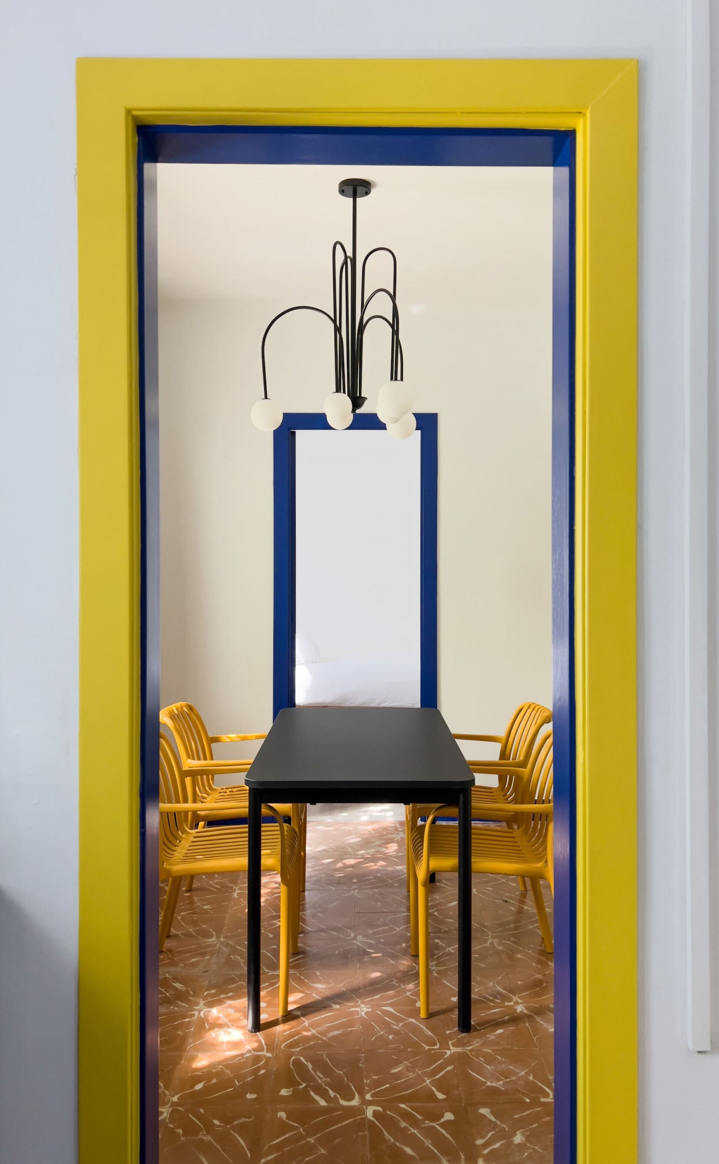 Una stanza con una porta a cornice gialla, un tavolo nero e sedie gialle.