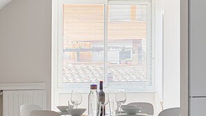 Un comedor con una mesa redonda, cuatro sillas, una ventana con persianas y un radiador.