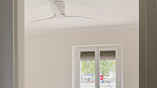 Una habitación limpia y blanca con una cama, un ventilador de techo y una puerta a un balcón.