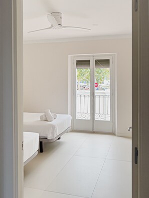 Ein sauberes, weißes Zimmer mit einem Bett, einem Deckenventilator und einer Balkontür.