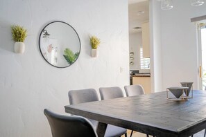 Un espace repas moderne avec une table en bois, des chaises grises, un miroir rond et deux plantes en pot.