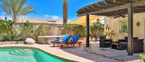 Una piscina con sillones de descanso, una pérgola y un patio amueblado.