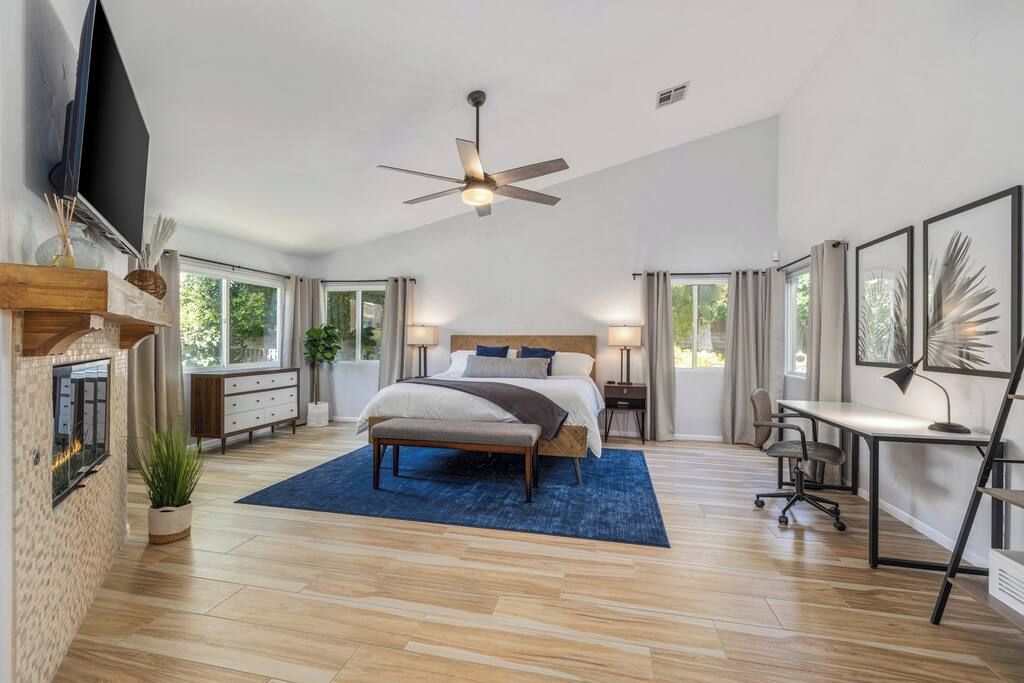Une chambre à coucher moderne, avec un lit, des tables de chevet, un bureau et un ventilateur de plafond.