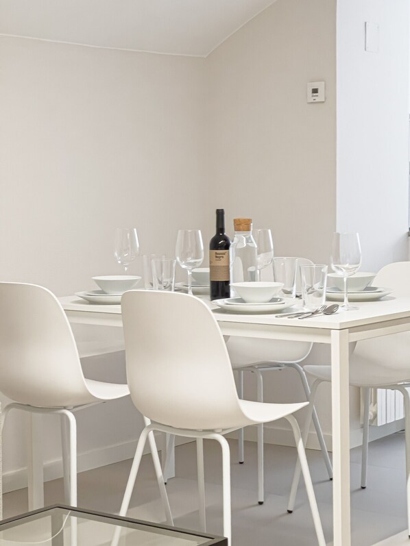 A dining area with a white table set for six, including wine glasses, plates, and cutlery.