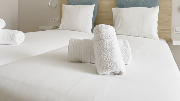 Una habitación de hotel con una cama grande, ropa blanca, dos almohadas y un cabecero de madera.