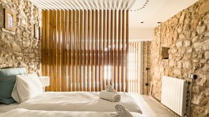 Una habitación de hotel moderna con una pared de piedra, una cama grande con ropa blanca y una partición de listones de madera.