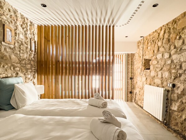 A modern hotel room with a stone wall, a large bed with white linens, and a wooden slatted partition.
