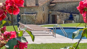 Un edificio de piedra con techo de tejas, piscina y sillas de descanso.