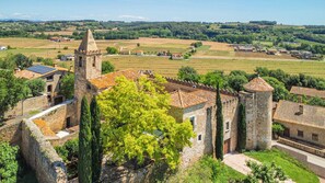A historic stone building with a tower, surrounded by lush greenery and fields.