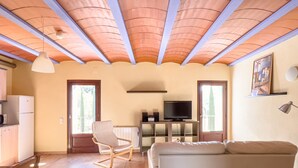 Ein Wohnzimmer mit Sofa, Fernseher, Sessel und Küchenzeile mit Kühlschrank und Mikrowelle.