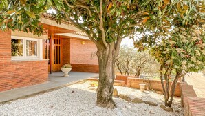A building with a brick exterior, a large tree in the foreground, and a gravel pathway leading to a wooden door.