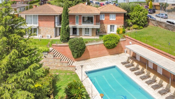 A two-story house with a swimming pool, a covered patio, and a well-maintained garden.
