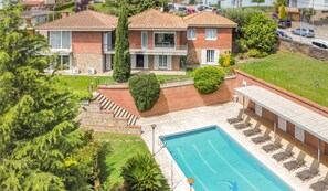A two-story house with a swimming pool, a covered patio, and a well-maintained garden.