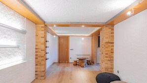 A hallway with wooden flooring, a black bean bag, a round wooden table with stools, and a door leading to another room.
