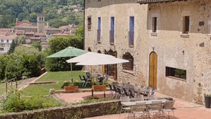 Un patio con mesas al aire libre, muros de piedra y vistas a un pueblo al fondo.